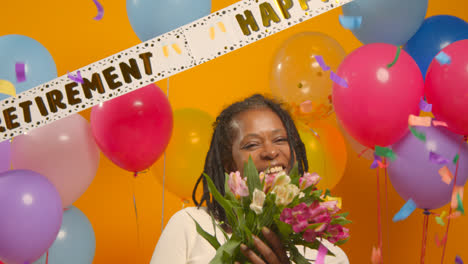 Studioporträt-Einer-Frau-Auf-Einer-Ruhestandsfeier,-Die-Einen-Blumenstrauß-Hält-Und-Mit-Luftballons-Feiert